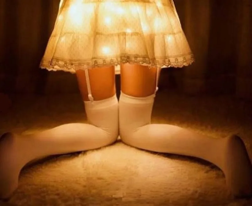 A person wearing white thigh-high stockings and a frilly, lace-trimmed skirt sits cross-legged on a carpeted floor, with the…