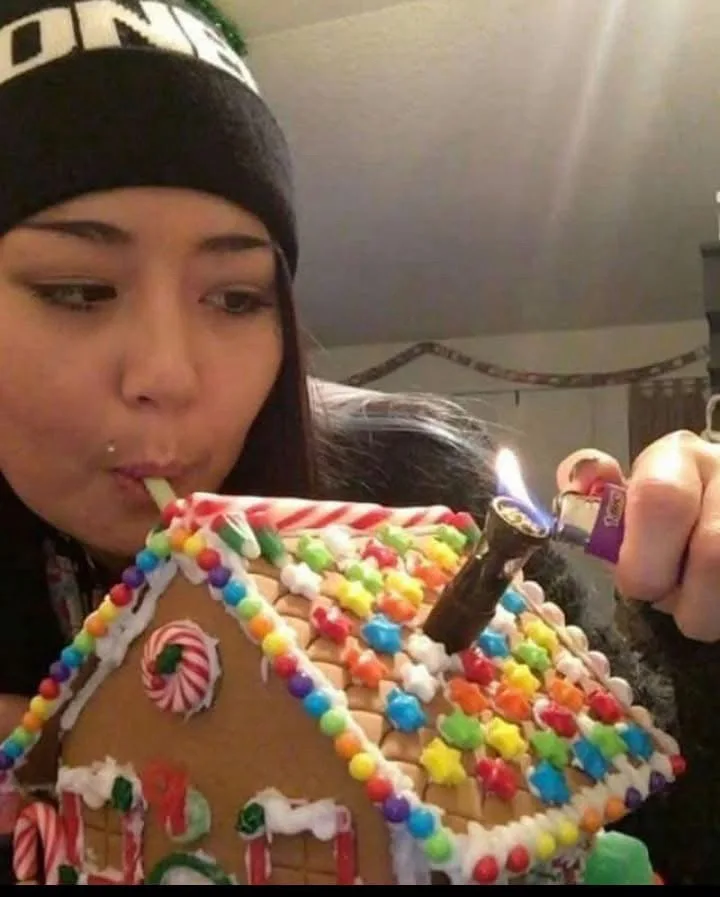A person wearing a black beanie with white lettering is blowing into a straw inserted into a colorful, elaborately decorated…