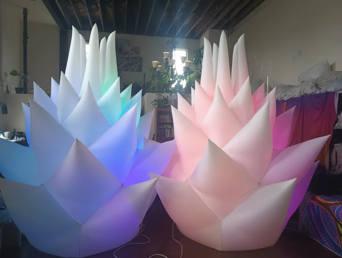 Two large, inflatable, lotus-shaped floor cushions sit side by side in a room; one glows with blue and purple lights, the…