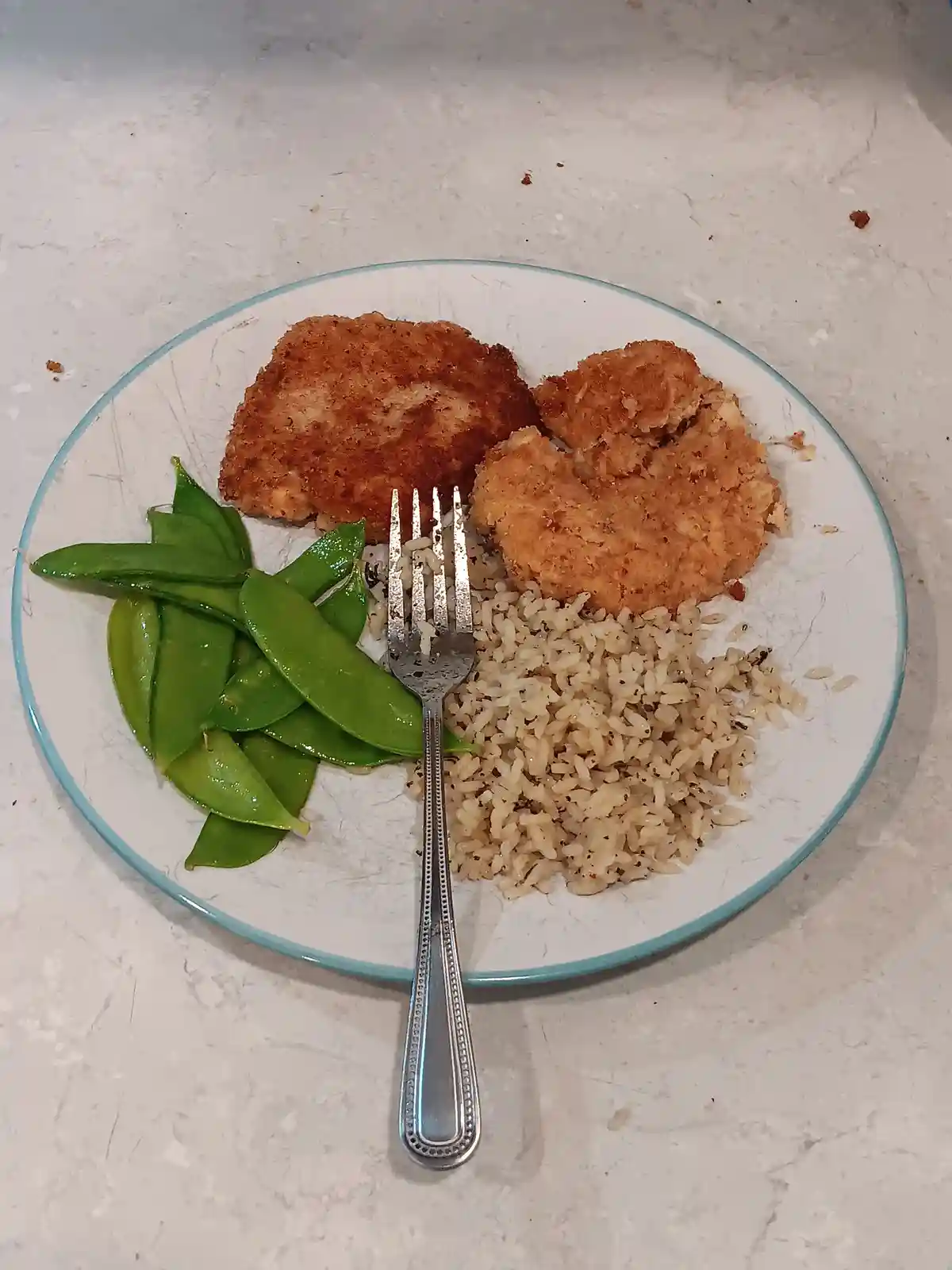 A plate of food with two golden-brown breaded chicken nuggets, a serving of brown rice, and a side of bright green snap…