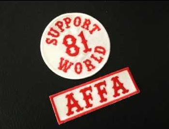 Two embroidered patches on a dark surface: a circular white patch with red text reading 'SUPPORT 81 WORLD' and a rectangular…