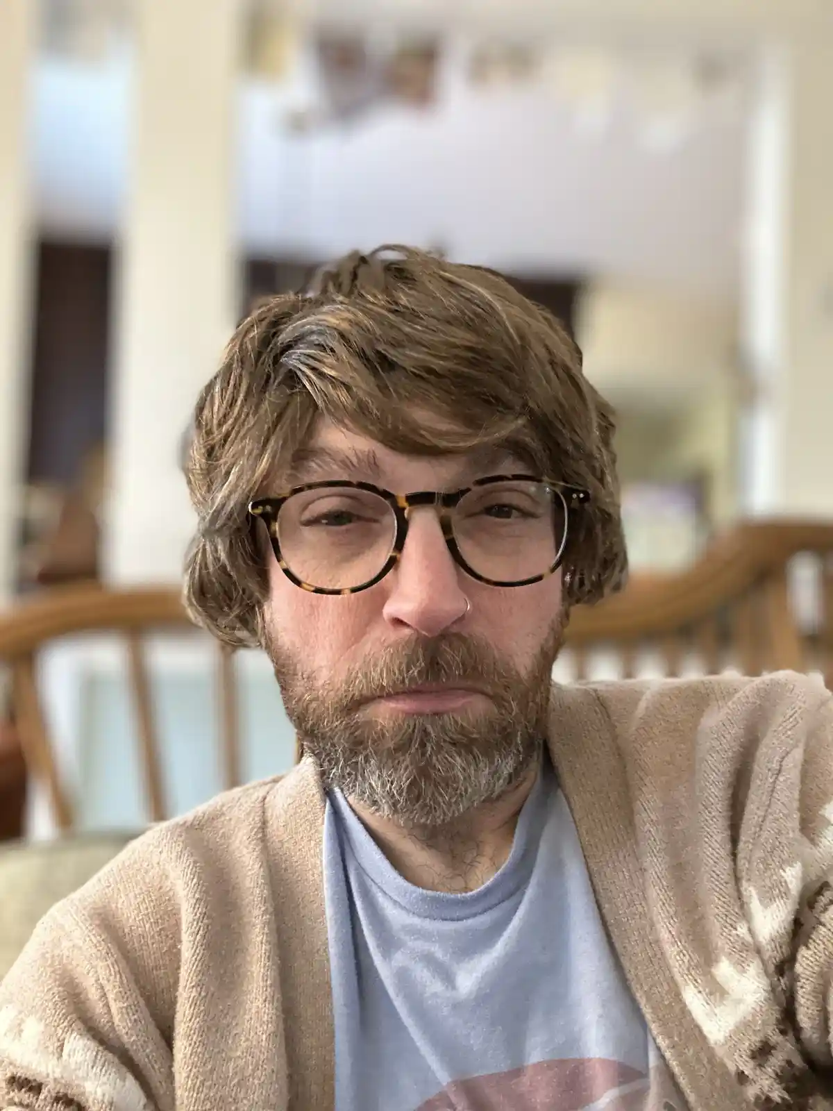 A man with brown hair, a beard with gray streaks, and tortoiseshell glasses stares directly at the camera with a weary…
