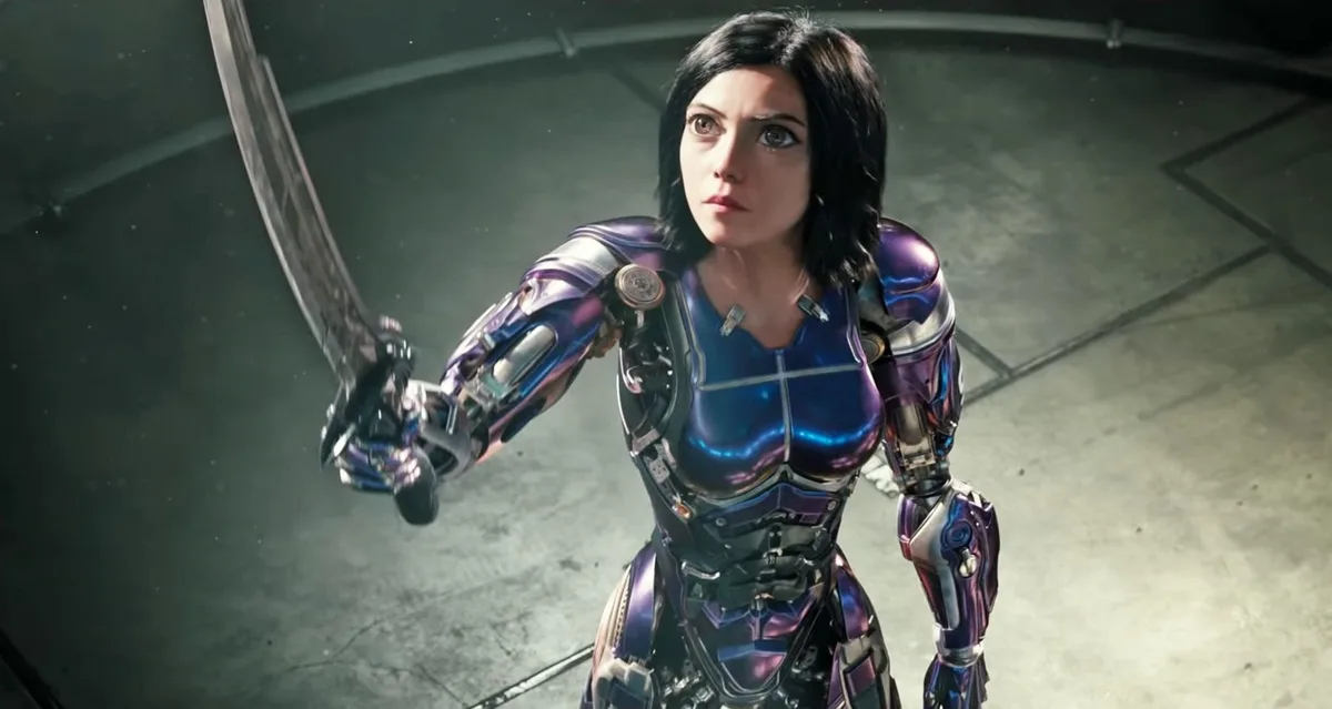 A female character in a shiny, metallic purple and blue armored suit holds a large sword in a combat stance, looking…