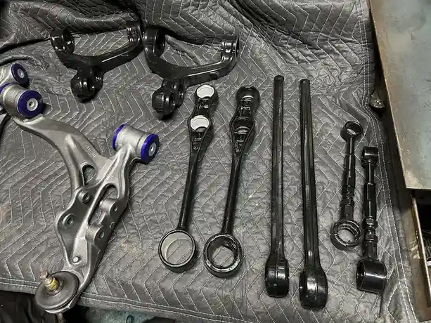 An overhead shot displays a collection of freshly painted black and silver automotive suspension components, including…