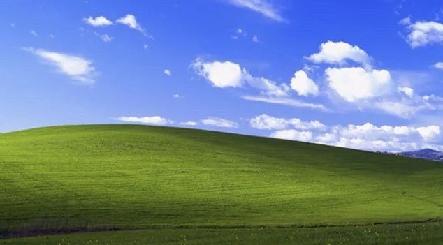 a famous green hill under a blue sky with white clouds, overlaid with the text 'the windows 98 wallpaper'. This image is…
