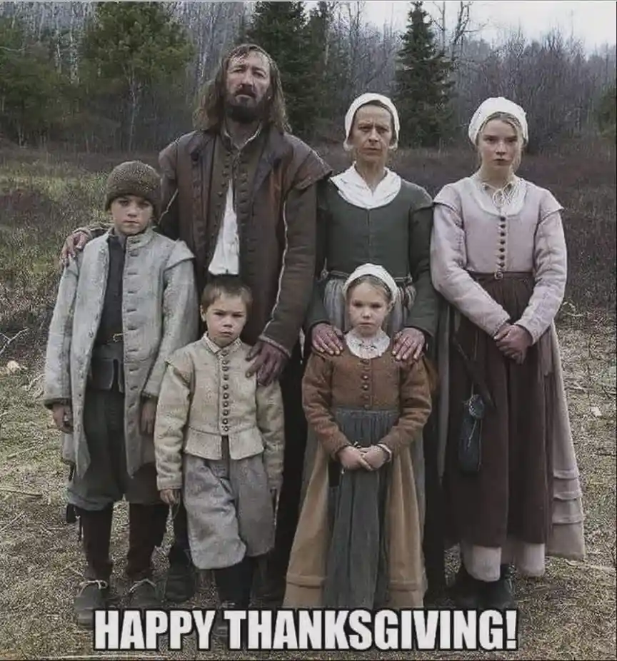 A family of six dressed in 17th-century Puritan-style clothing stands outdoors in a wooded area, all with stern, unsmiling…