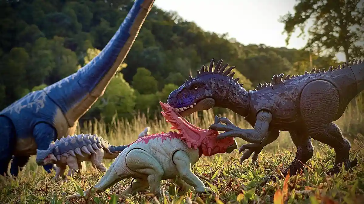 A photo of several plastic dinosaur toys arranged in a grassy field with trees in the background. A large blue dinosaur toy…