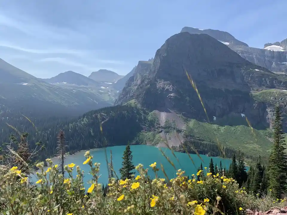 A scenic mountain landscape featuring a turquoise alpine lake nestled among towering, rocky peaks with patches of snow. The…