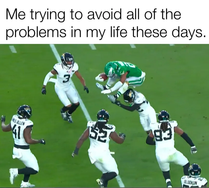 A football player in a green jersey leaps high while holding a football, surrounded by several opposing players in white…