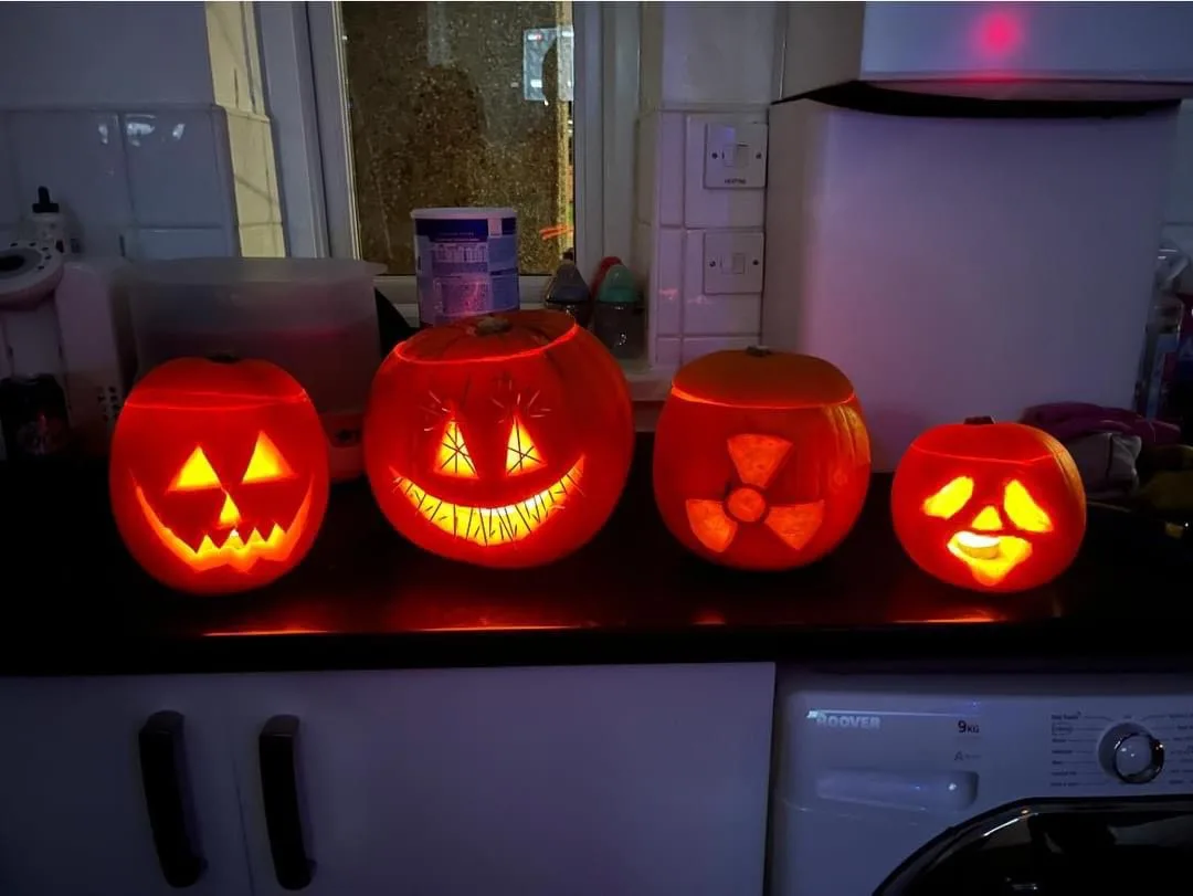 Four glowing jack-o'-lanterns sit on a kitchen counter, each with a different carved face: a classic scary grin, a wide…