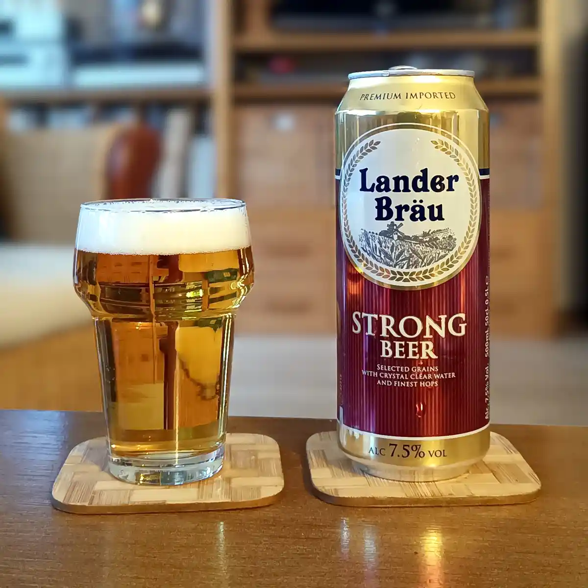 A can of Lander Bräu Strong Beer, labeled with 7.5% alcohol, sits next to a glass filled with the same beer on wooden…