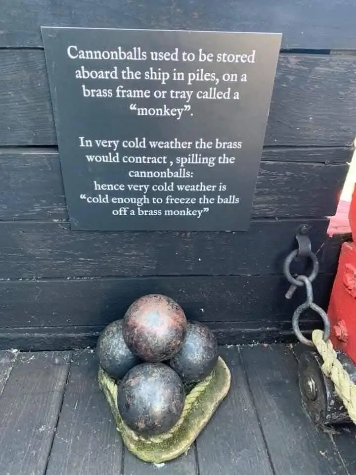 A black plaque mounted on dark wooden planks explains the origin of the idiom 'cold enough to freeze the balls off a brass…