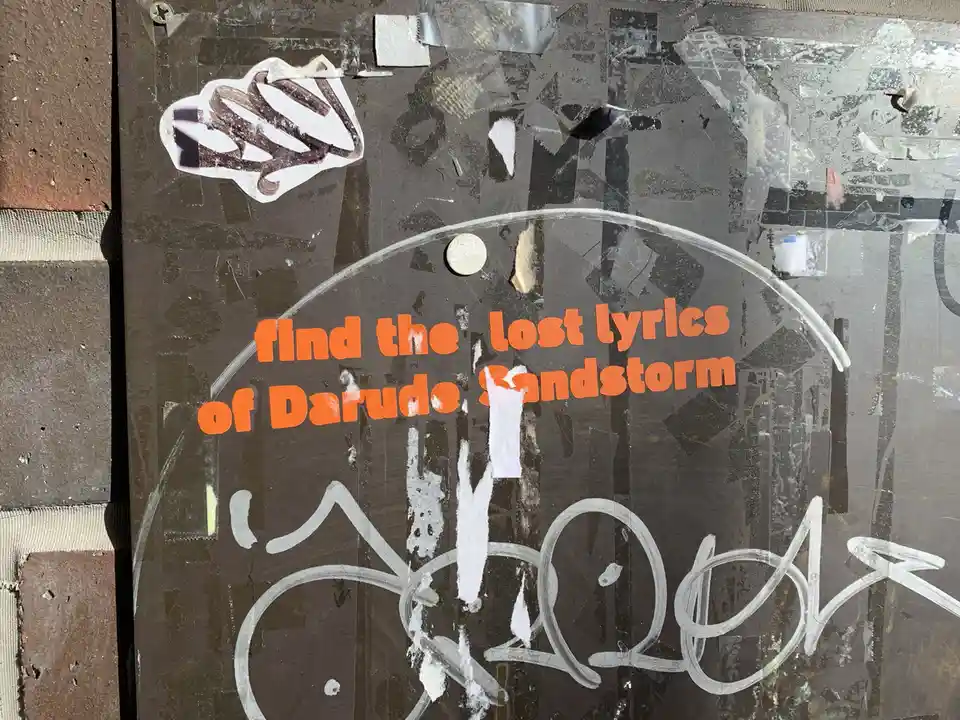 A close-up of a weathered, graffiti-covered surface with peeling stickers and tape. Prominent orange text reads 'find the…