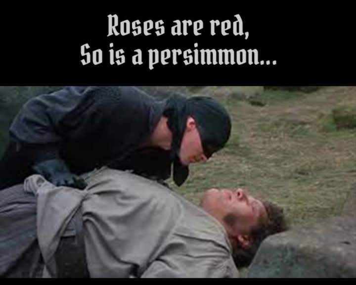 A man in a black hooded outfit leans over another man lying on the ground in a grassy outdoor setting. The overlaid text…