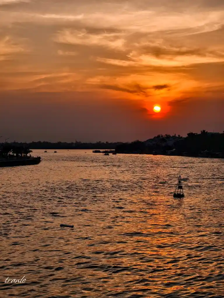 A serene sunset over a body of water with the sun low on the horizon, casting orange and red hues across the sky and…