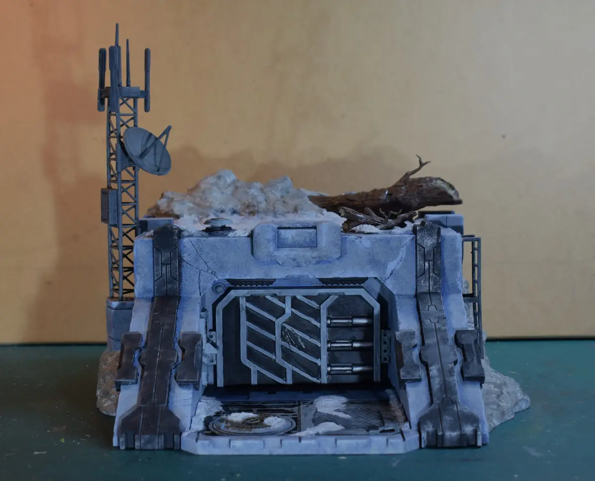 A detailed miniature sci-fi bunker model with a large door, satellite tower, and rocky terrain, overlaid with the text 'i…