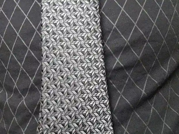 A close-up photo shows a gray suit jacket with a diagonal pinstripe pattern, with a gray and white geometric-patterned tie…