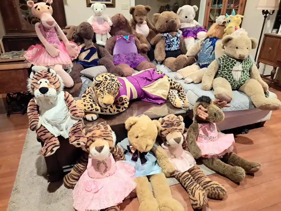A large collection of stuffed animals, including bears, tigers, and a giraffe, are arranged on a couch and floor in a living…