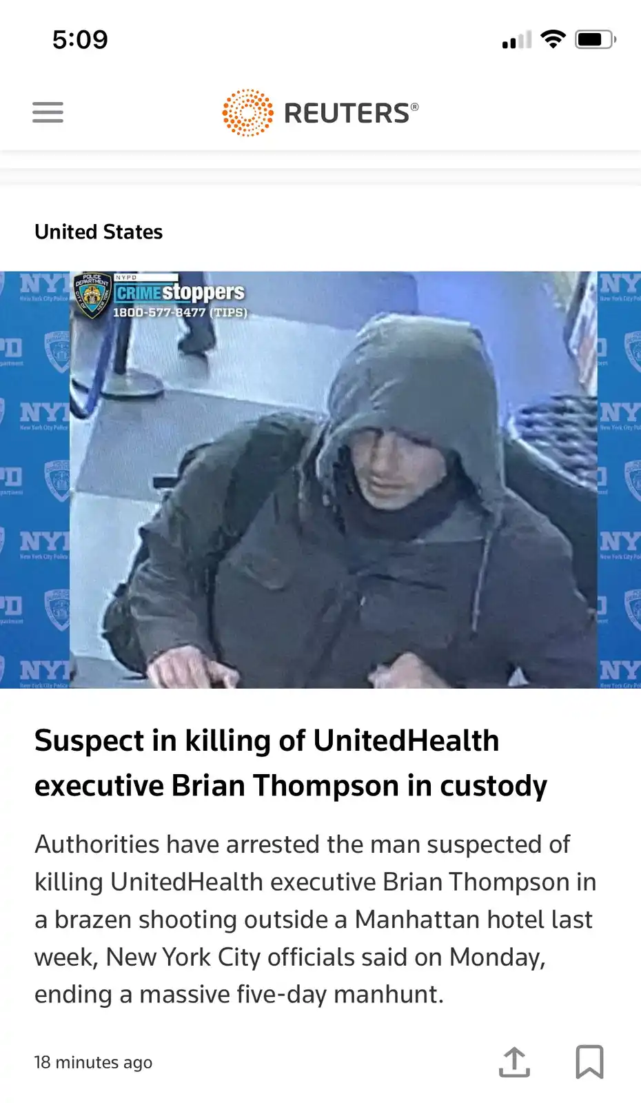 A grainy security camera image shows a person wearing a dark hooded jacket and a dark beanie, looking down. The image is…