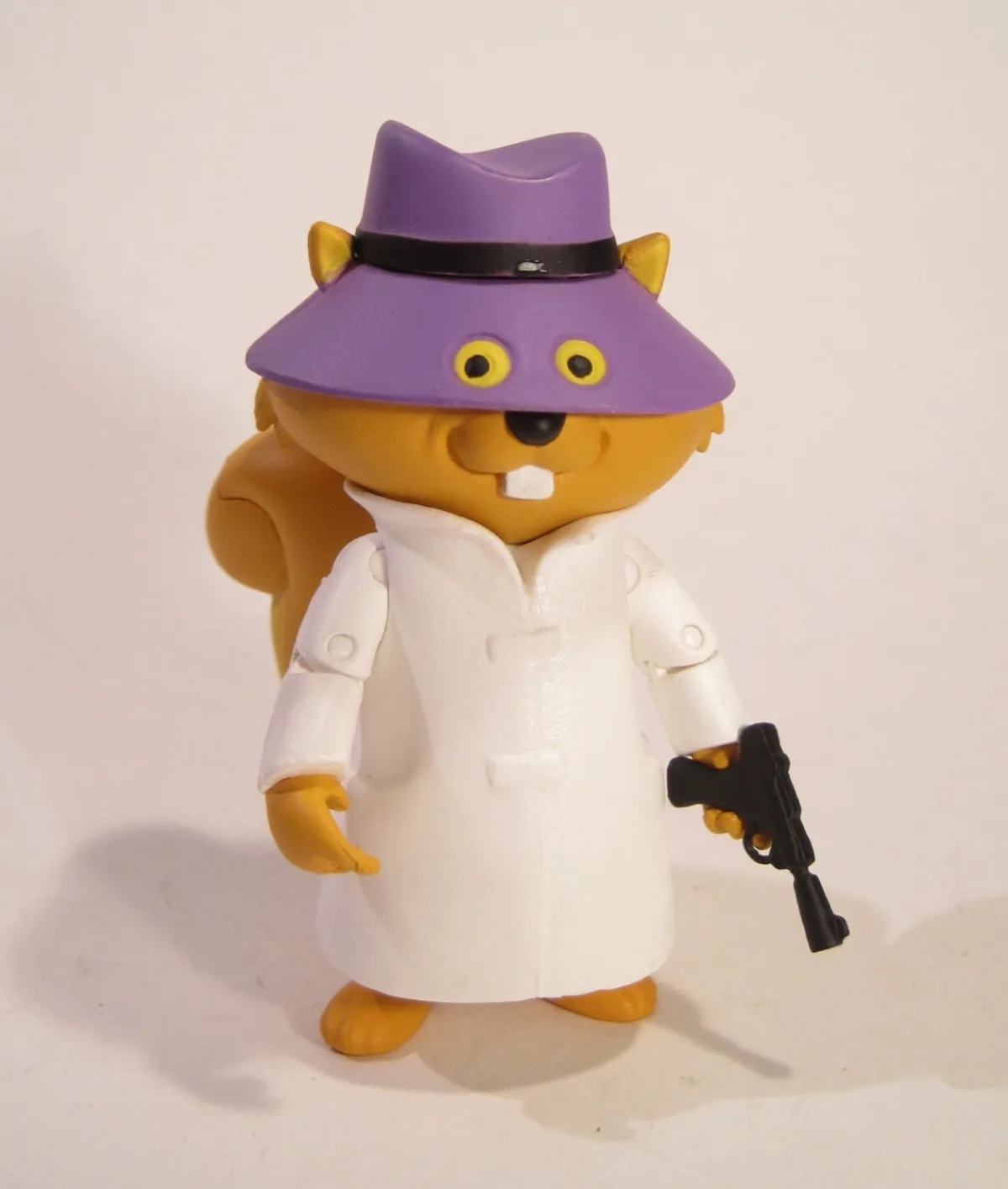 A plastic toy figure of a cartoon beaver wearing a purple fedora with a black band, a white trench coat, and holding a black…