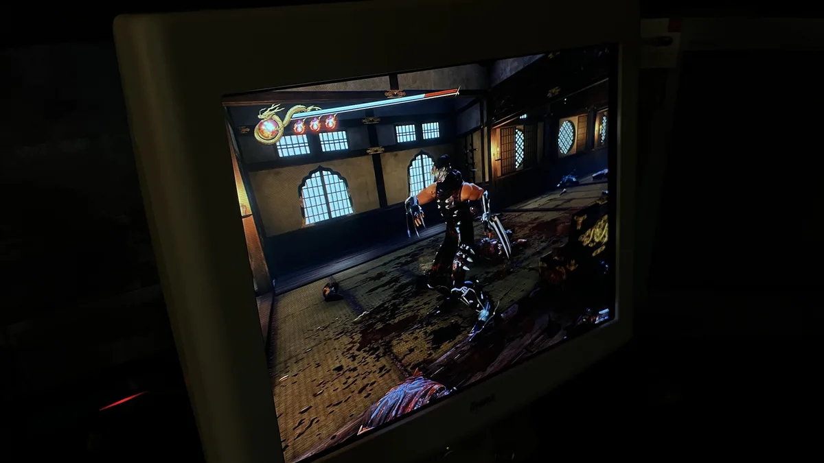 A photo of a computer monitor in a dark room displaying a violent video game scene with a masked character standing over a…
