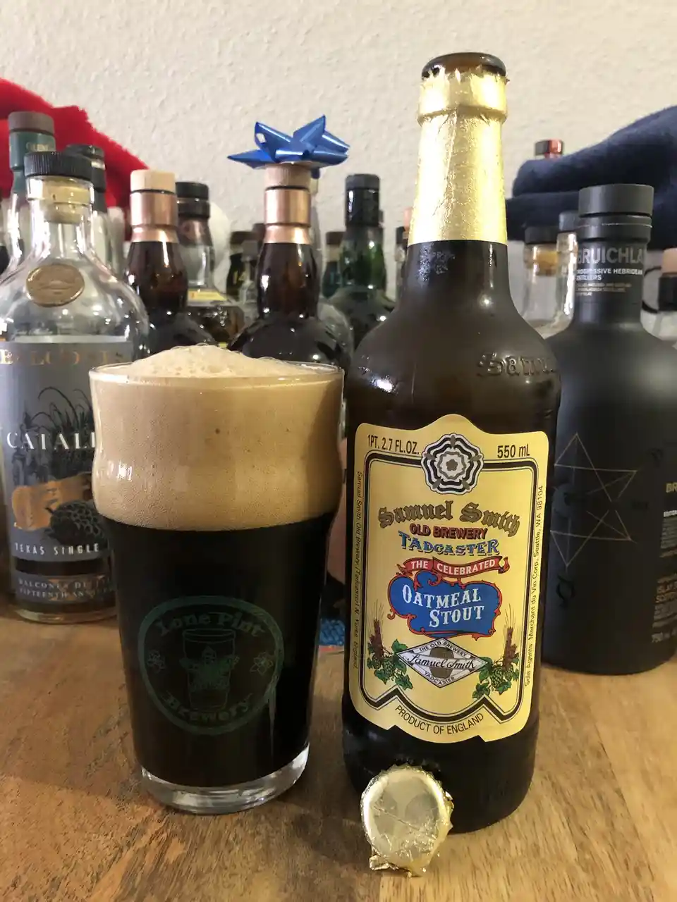 A bottle of Samuel Smith Old Brewery Tadcaster Oatmeal Stout sits next to a full glass of the dark beer with a thick head…