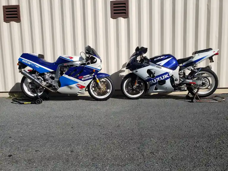 Two Suzuki GSXR sport motorcycles, one a 750 model with Yoshimura branding and the other a later model, are parked side by…