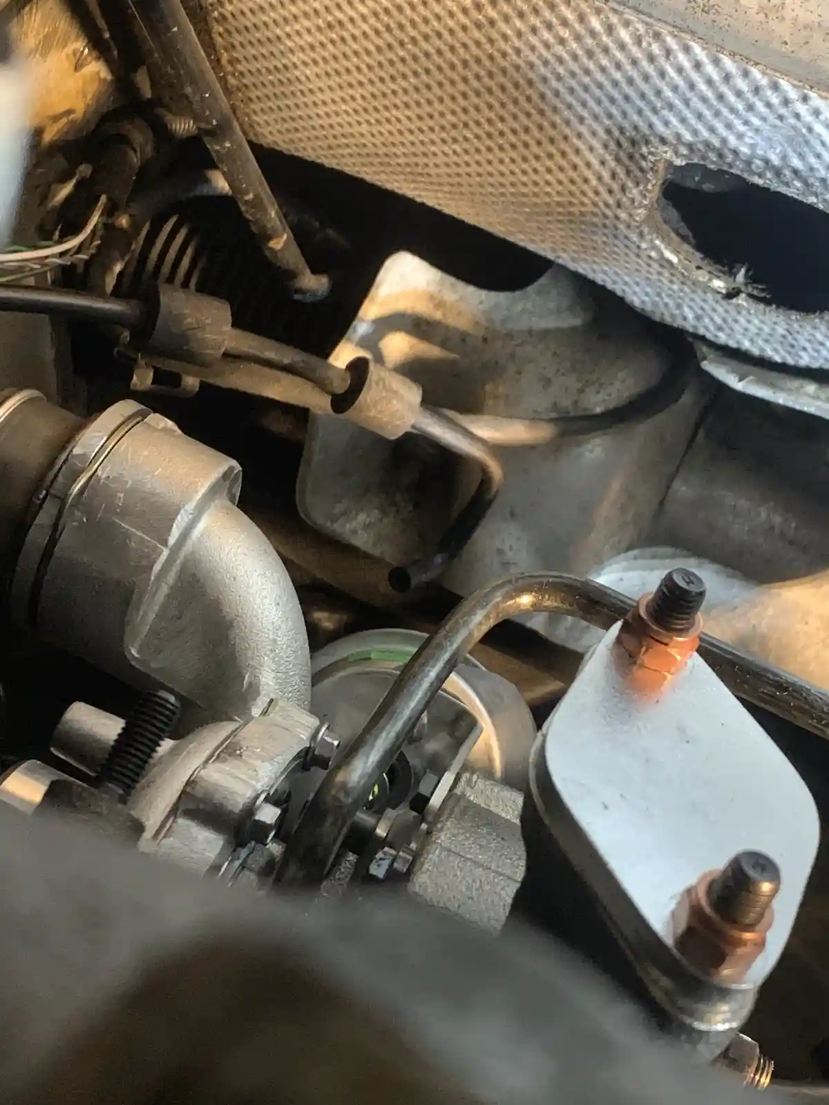 A close-up photo of a car's engine bay showing various mechanical parts, hoses, and metal components, with the overlaid text…