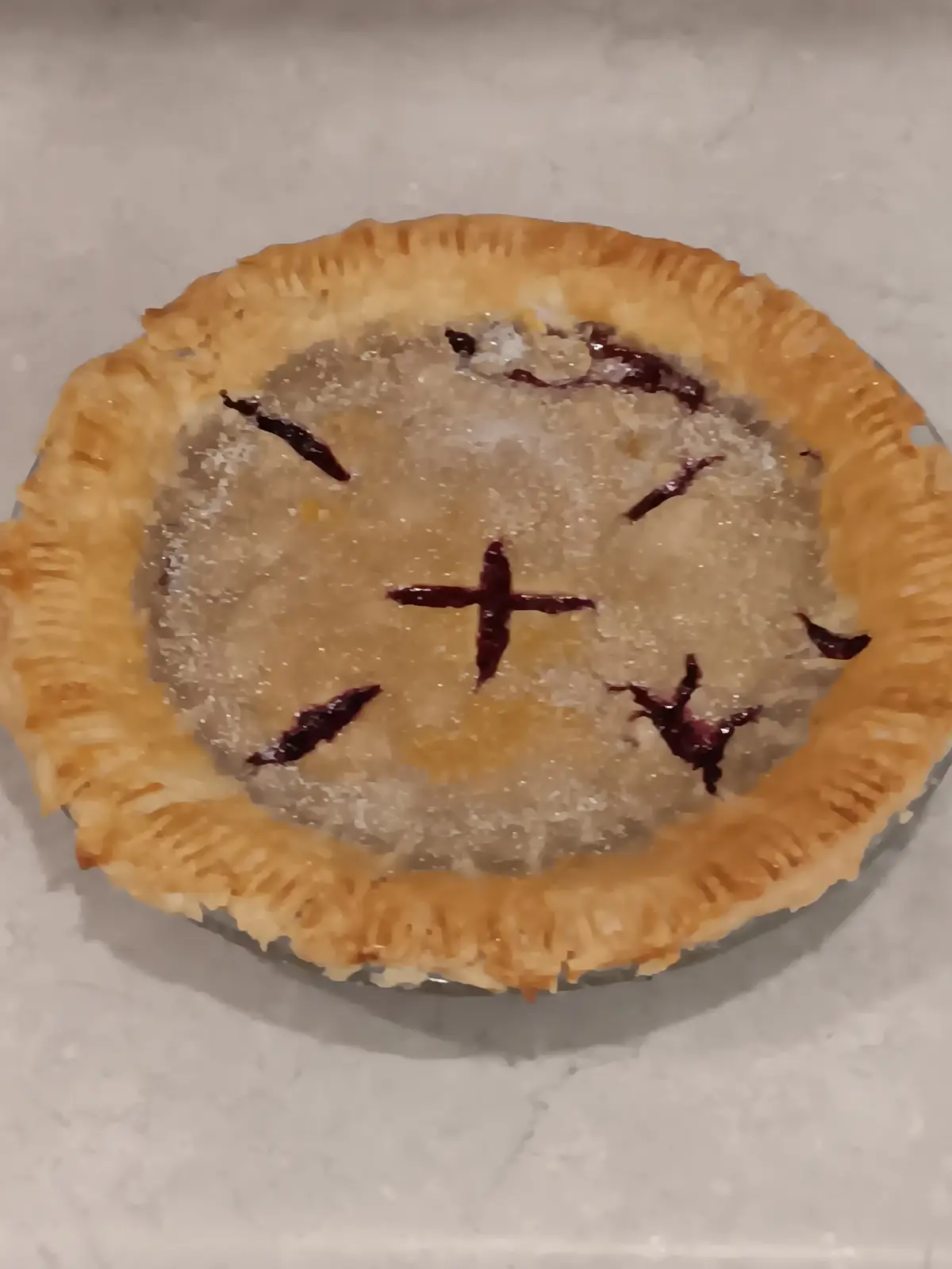 A close-up photo of a baked pie with a golden-brown crust and sugar crystals on top. The pie's filling is visible through…