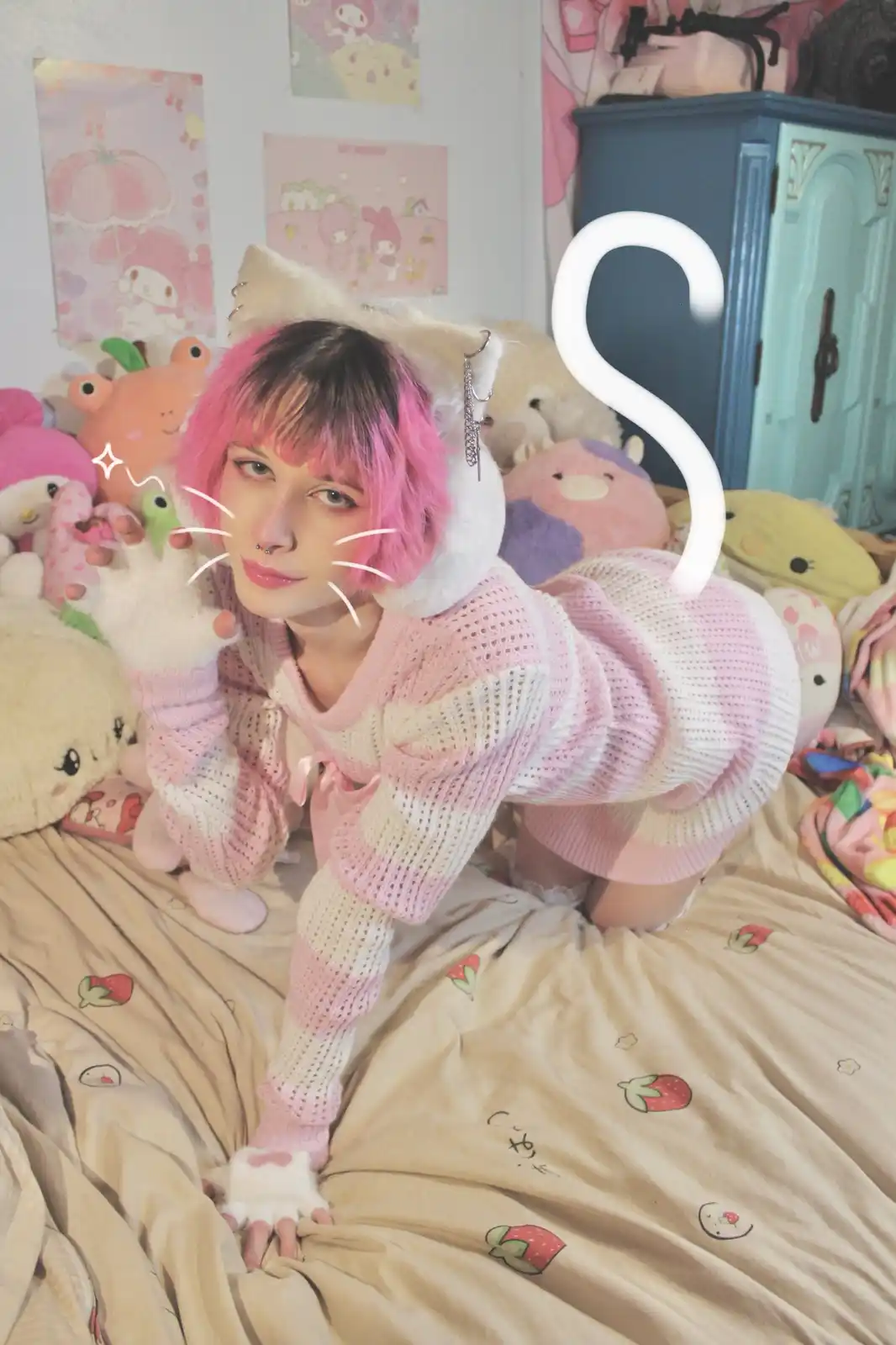 A person with pink hair and cat ears poses on a bed surrounded by plush toys and kawaii decor, wearing a pink and white…