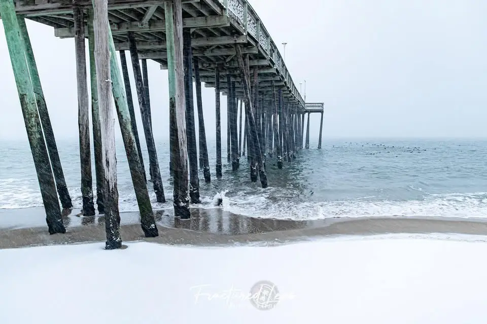A photograph of a wooden pier extending over a foggy ocean, with waves lapping at the shore. The foreground is covered in…