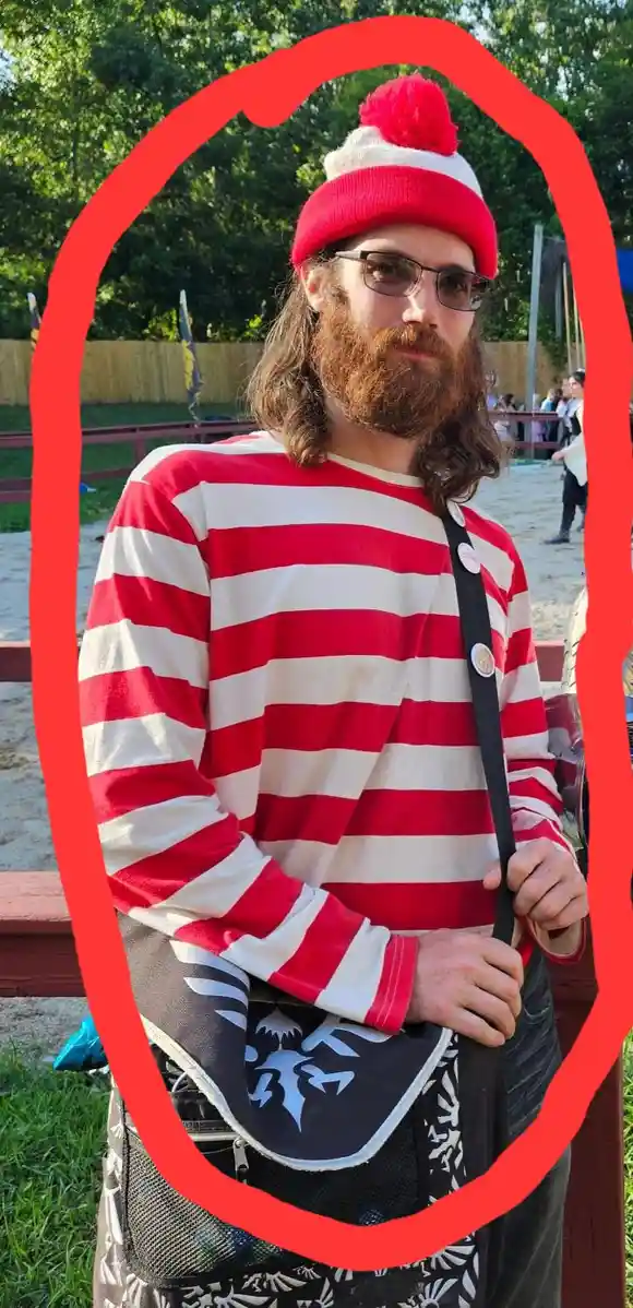 a man with a long brown beard and glasses wears a red and white striped shirt and a red and white beanie with a red pom-pom…