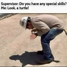 A man wearing a white hard hat and work clothes is bent over on a dirt ground, gesturing toward his shadow which resembles a…