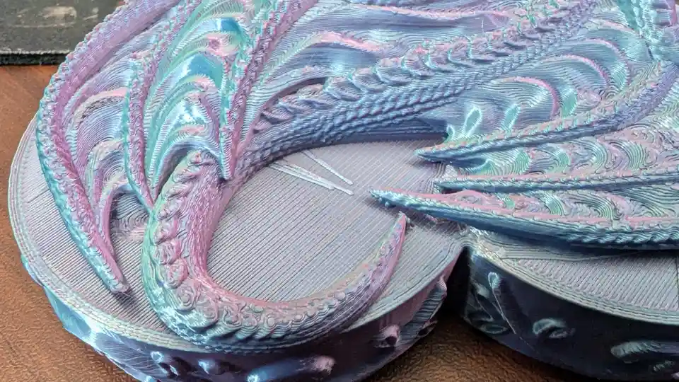 A close-up of a 3d-printed dragon sculpture with iridescent purple and teal scales, showing its coiled body and detailed…