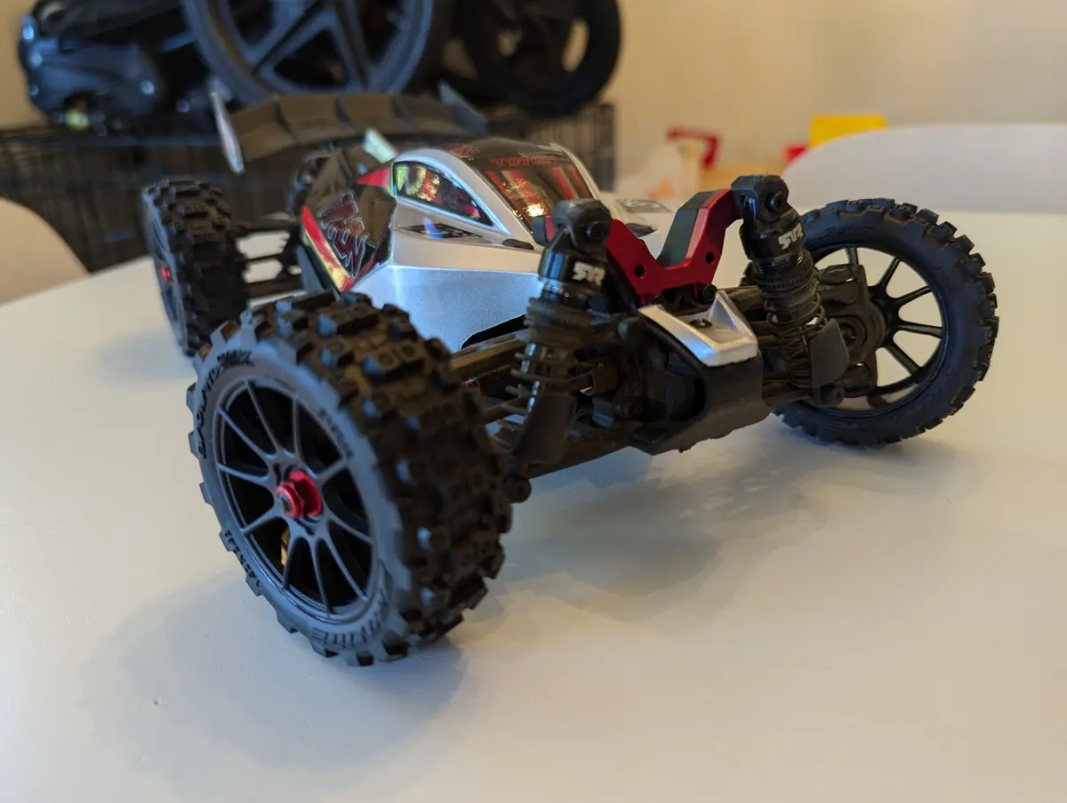 A close-up photo of a detailed silver and red remote-controlled monster truck with large knobby tires and visible suspension…