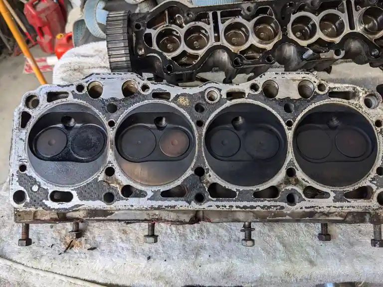 Two engine cylinder heads are shown side by side on a towel; the top one is clean and shiny with visible valve seats, while…