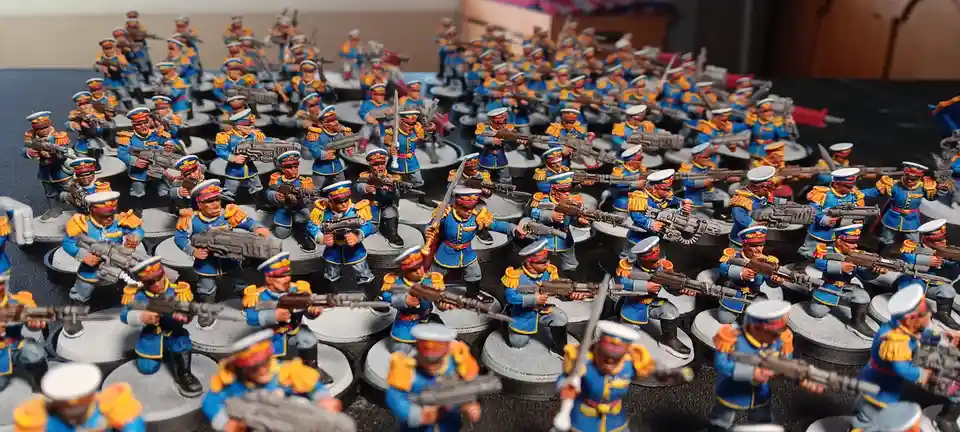 A large collection of painted miniature figurines depicting soldiers in blue uniforms with yellow epaulets and white hats…