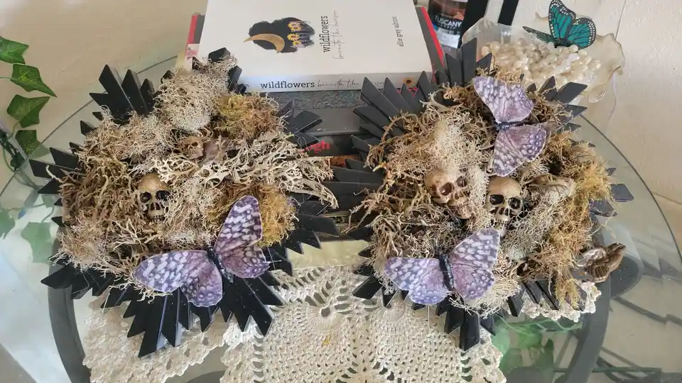 Two decorative black hedgehog-shaped objects are filled with dried moss, small skulls, and purple patterned butterflies…