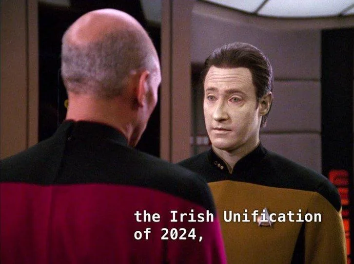 A still from Star Trek: The Next Generation shows Captain Picard (back to camera, in a red uniform) facing Commander Worf…
