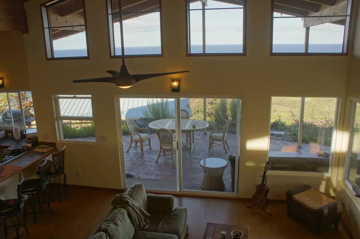 A spacious, well-lit open-plan living area with hardwood floors, a sofa, and a kitchen bar, featuring numerous large windows…