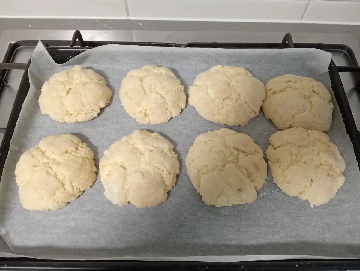 Eight pale, lumpy, misshapen baked goods sit on a parchment-lined baking tray on a stovetop, looking like failed attempts at…