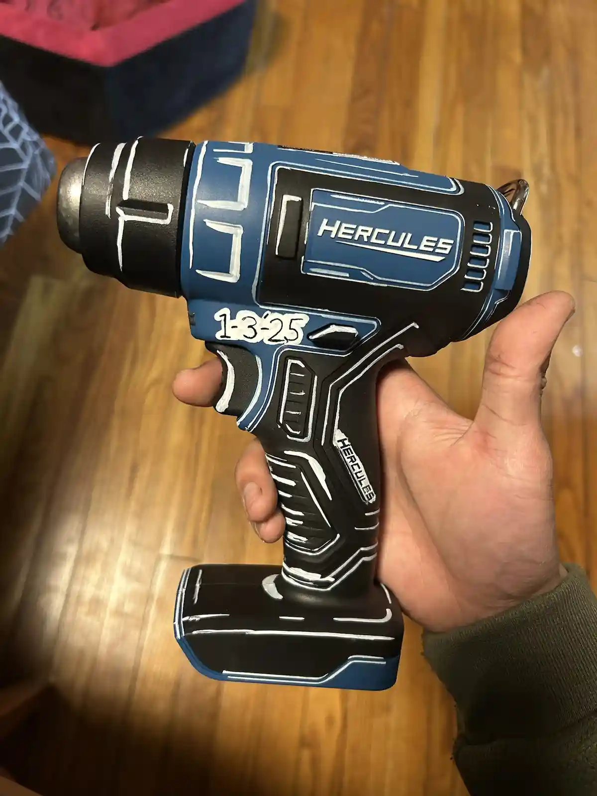 A hand holds a blue and black power tool, resembling a drill or impact driver, with 'HERCULES' branding. The tool has been…