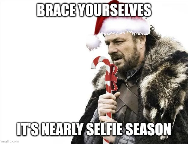 A man with a beard and fur-lined coat, wearing a red and white Santa hat and holding a candy cane, looks grimly at the…