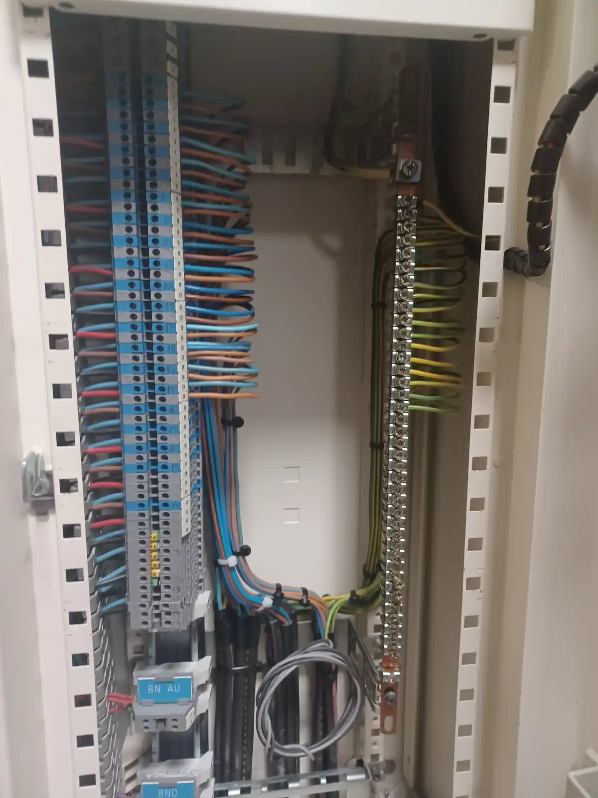 An open electrical panel filled with neatly organized colorful wires connected to terminal blocks, with overlaid text…