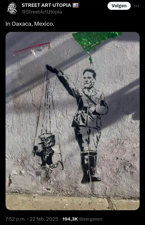 A black-and-white street art mural on a textured wall depicts a man in a military-style uniform holding strings that control…
