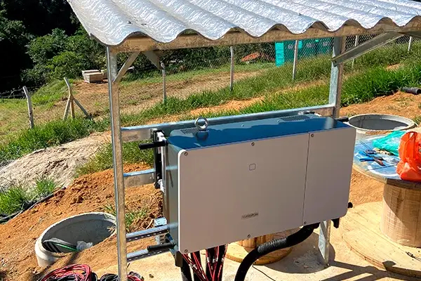 a blue and silver solar inverter is mounted under a corrugated metal roof in an outdoor dirt area, with wires connected and…