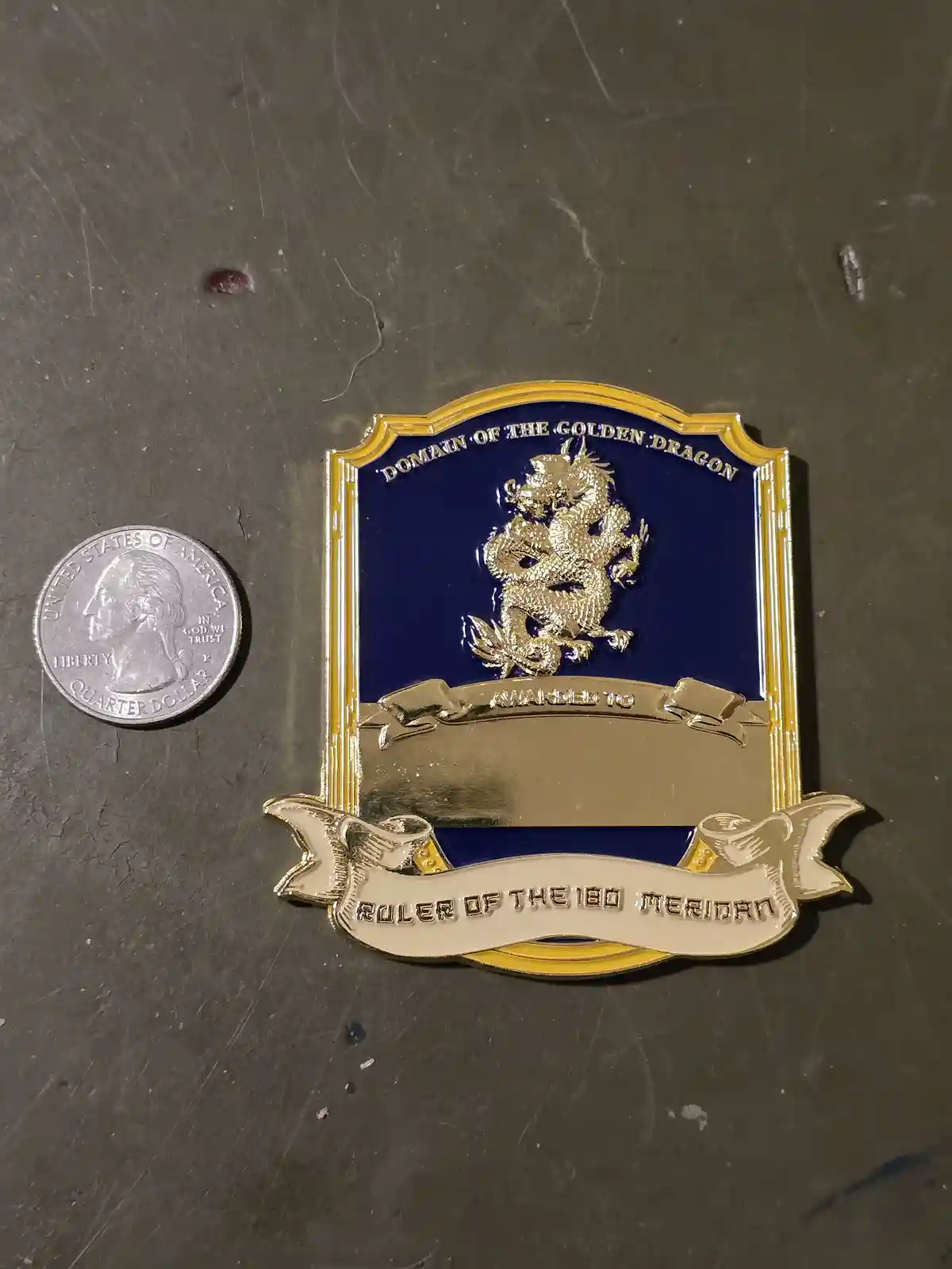 A close-up photo shows a decorative pin with a blue background and a gold dragon emblem, placed next to a U.S. quarter for…