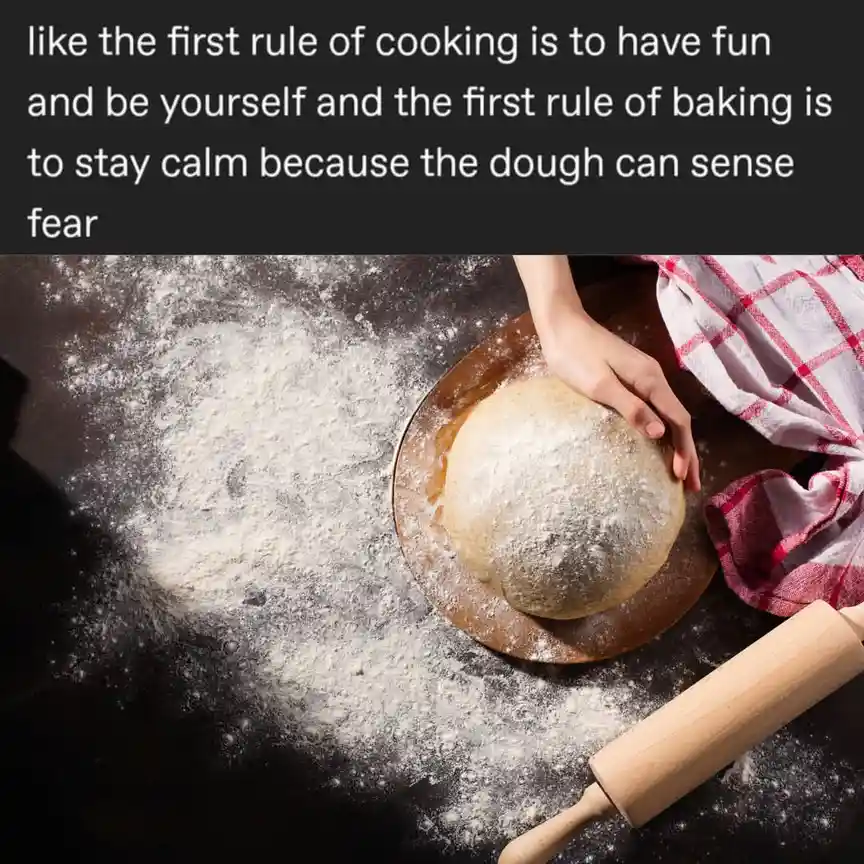 A top-down photo shows a hand holding a round ball of dough on a wooden board, surrounded by flour on a dark surface, with a…