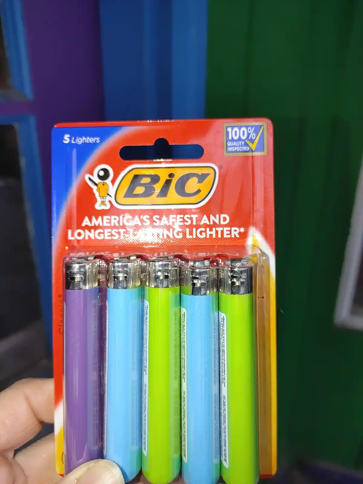 A hand holds a pack of five colorful BIC lighters in purple, blue, and green, with the packaging prominently displaying the…