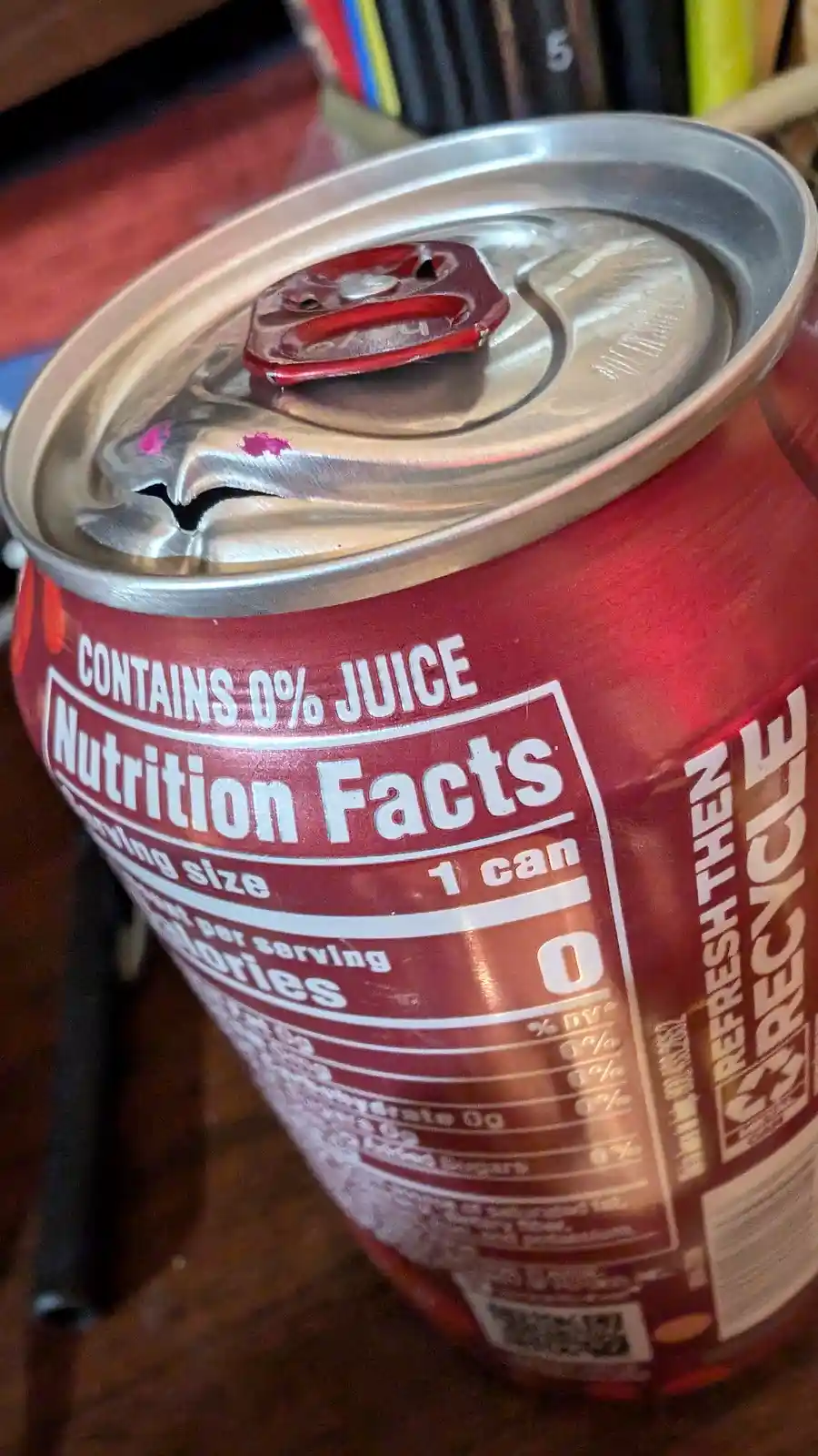 A close-up photo of an opened red soda can showing its nutrition label, which reads 'CONTAINS 0% JUICE' and '0 Calories' per…